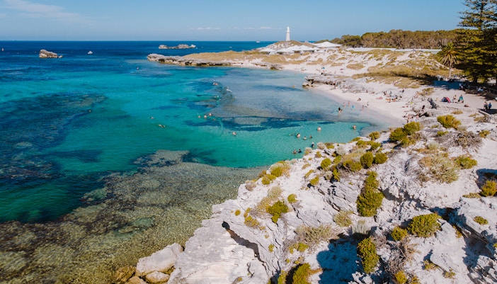 Tourists swimming at a beach on Rottnest Island with a lighthouse in the distance.