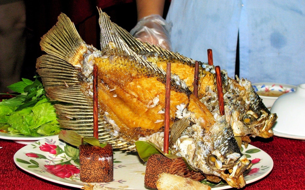 Fried fish served on a plate with greens during Mekong Delta Full Day Tour.