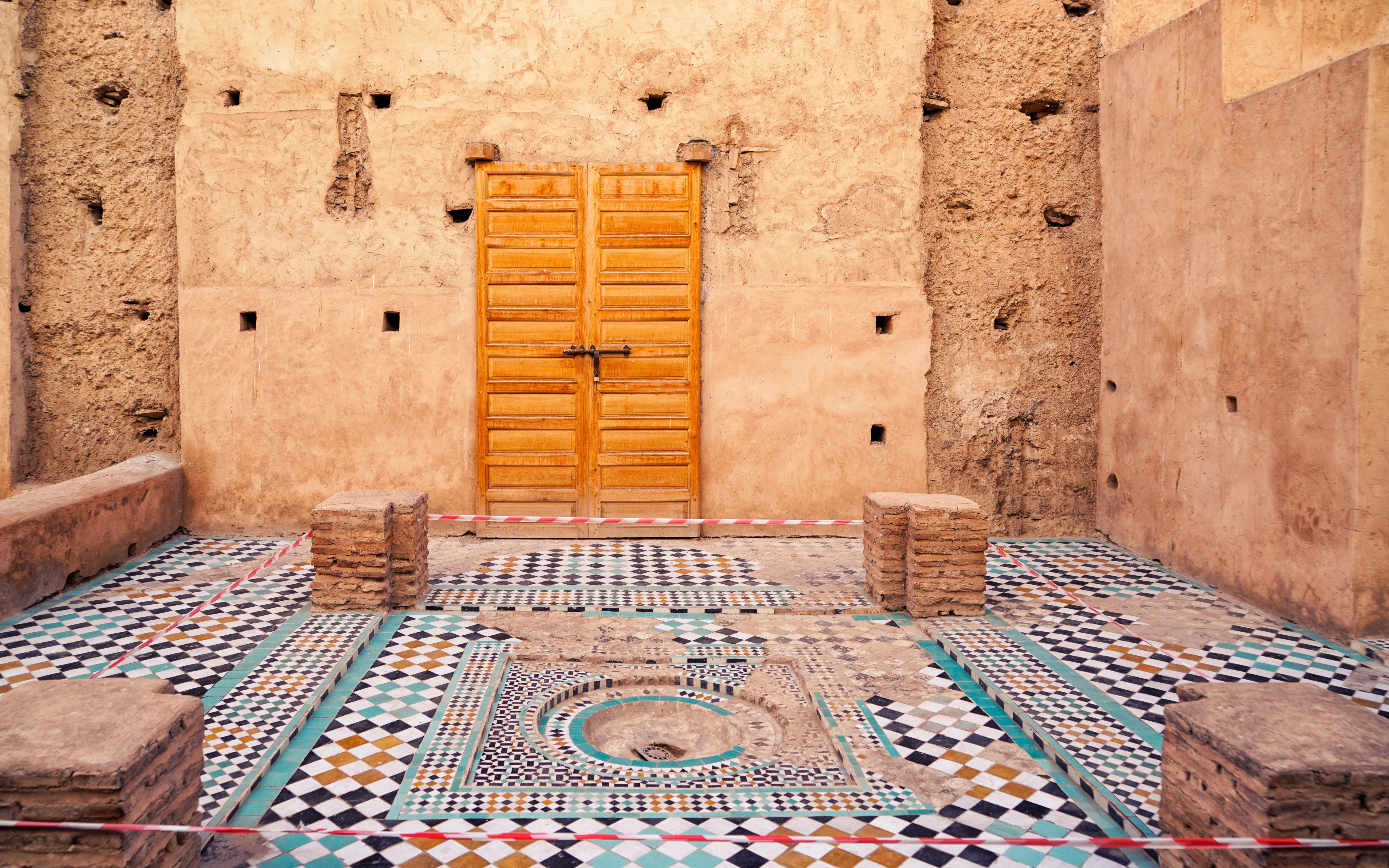 Courtyard with mosaic tiles and wooden door in Badi Palace, Marrakesh, Morocco.
