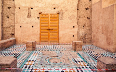 Courtyard with mosaic tiles and wooden door in Badi Palace, Marrakesh, Morocco.
