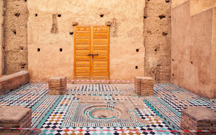 Courtyard with mosaic tiles and wooden door in Badi Palace, Marrakesh, Morocco.