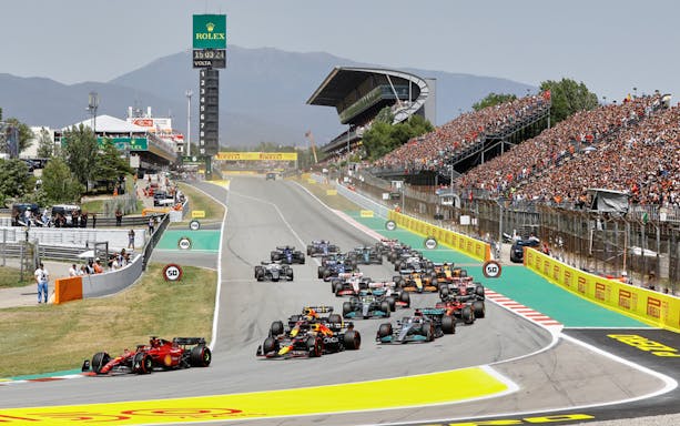 Formula 1 cars racing at Circuit de Barcelona-Catalunya with packed grandstands.