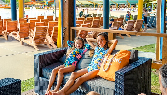 Family relaxing in cabana at Whitewater World with poolside view.