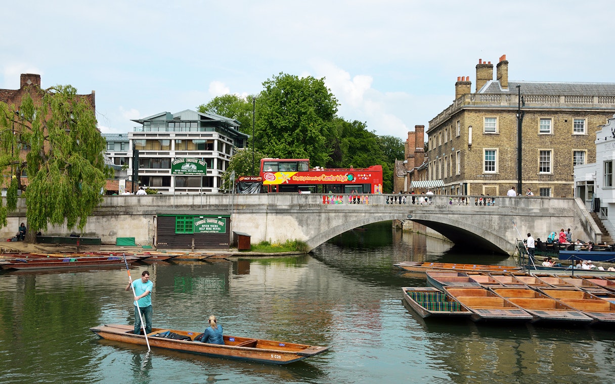 Cambridge Hop-On Hop-Off bus crossing a bridge over the River Cam with punting boats below.