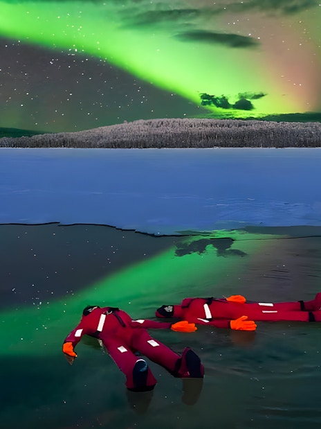 Person ice floating under Northern Lights in Rovaniemi.