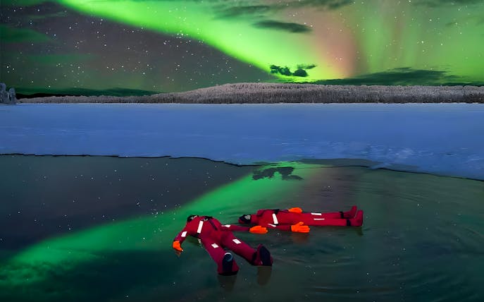 Person ice floating under Northern Lights in Rovaniemi.