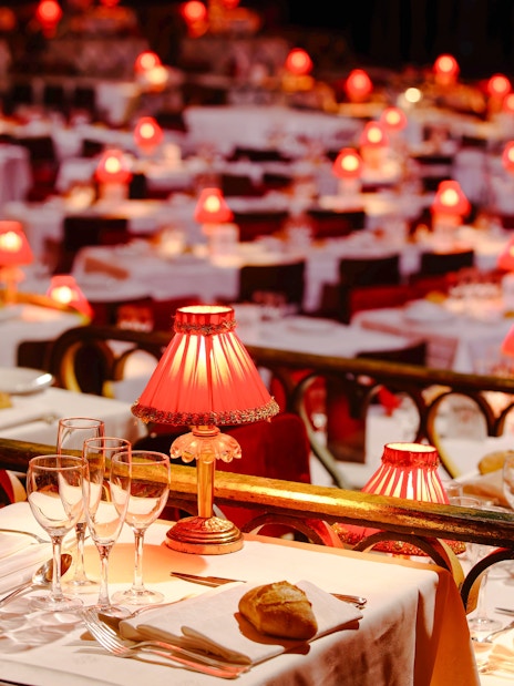 Elegant dining setup with red lamps at Moulin Rouge Show, Paris.