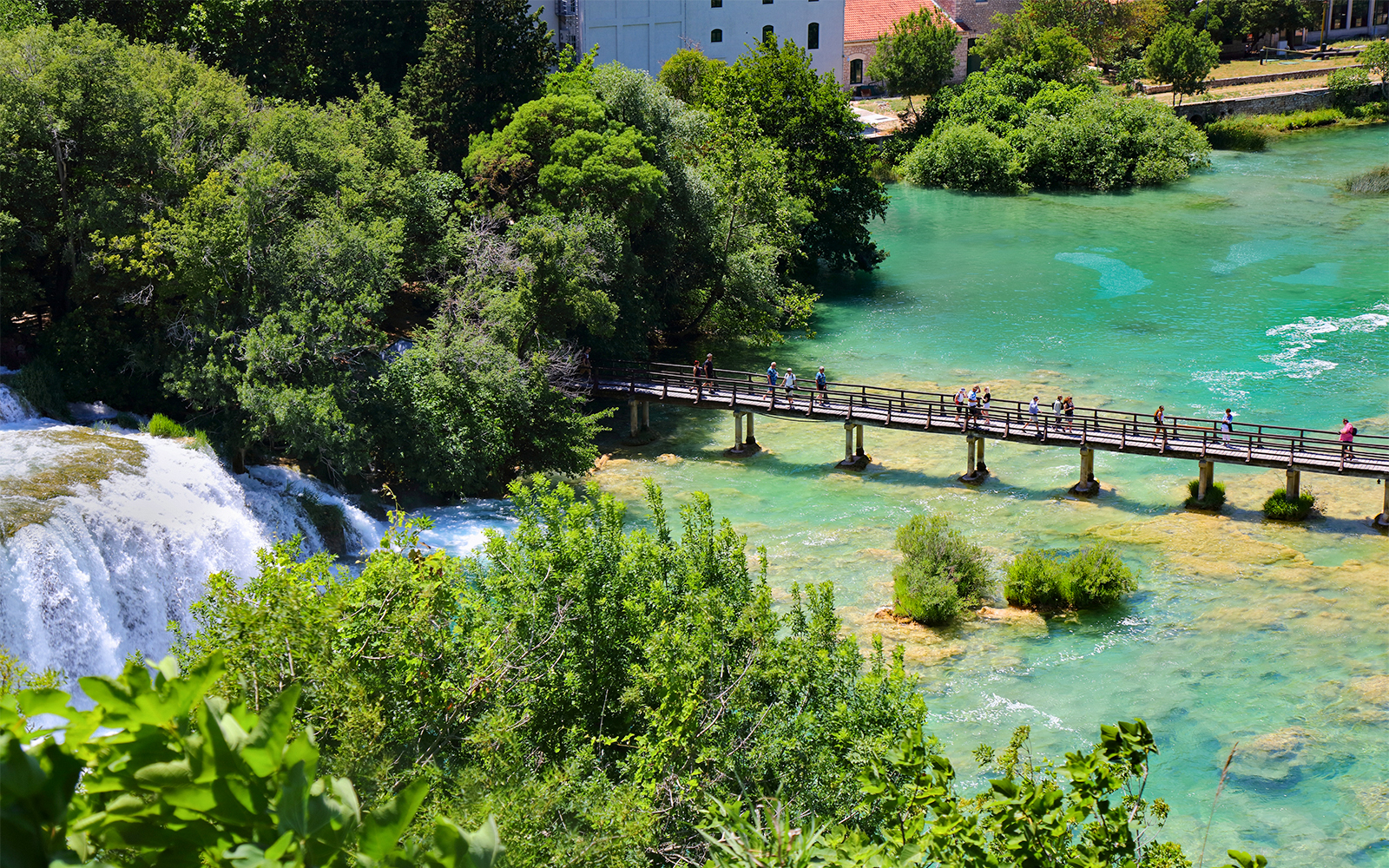 Visitors crossing a wooden bridge over waterfalls at Krka National Park, Croatia.