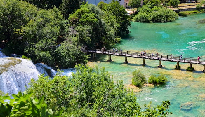 Visitors crossing a wooden bridge over waterfalls at Krka National Park, Croatia.