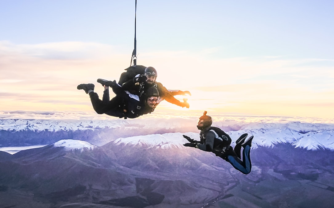 Skydivers above Mt Cook with snow-capped mountains at sunrise.