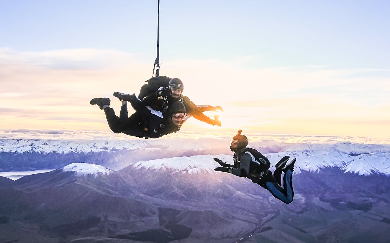 Skydivers above Mt Cook with snow-capped mountains at sunrise.