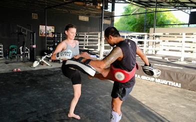 Beginner practicing Muay Thai kick with instructor in Krabi gym.