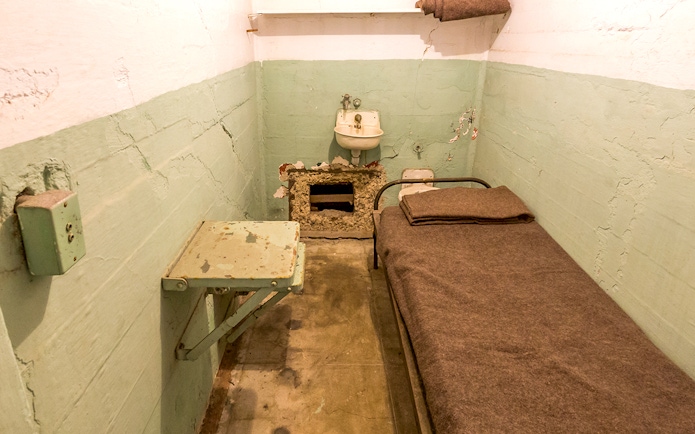 Alcatraz prison cell interior with bed, sink, and small table at night.