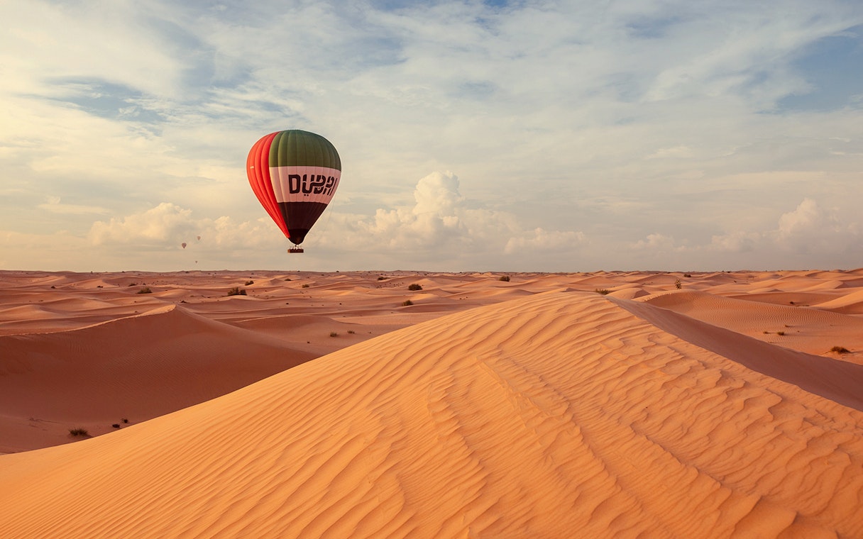 Hot air balloon over Dubai desert dunes during premium tour experience.