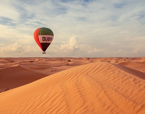 Hot air balloon over Dubai desert dunes during premium tour experience.