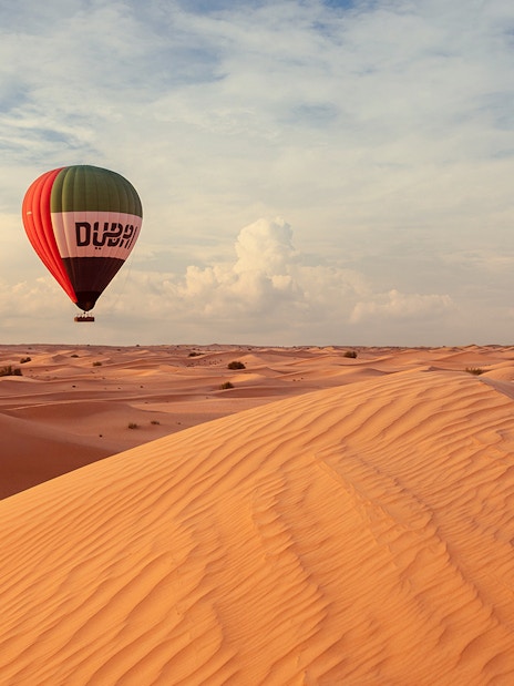 Hot air balloon over Dubai desert dunes during premium tour experience.
