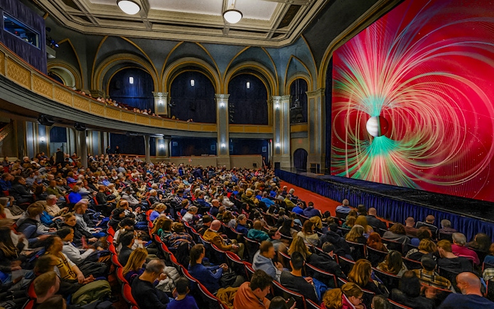 Audience watching a space-themed presentation at the American Museum of Natural History.