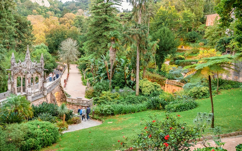 Quinta da Regaleira garden with tourists exploring lush greenery and ornate stone structure.