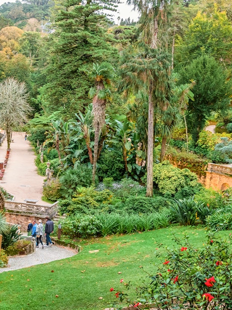 Quinta da Regaleira garden with tourists exploring lush greenery and ornate stone structure.