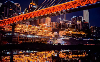 Chongqing cityscape at night with illuminated bridge and skyline reflections.