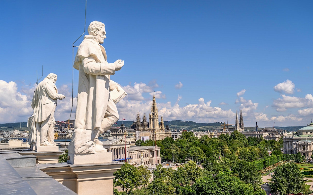 Statues on the rooftop of Natural History Museum Vienna with cityscape view.