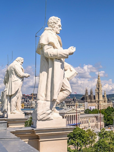 Statues on the rooftop of Natural History Museum Vienna with cityscape view.