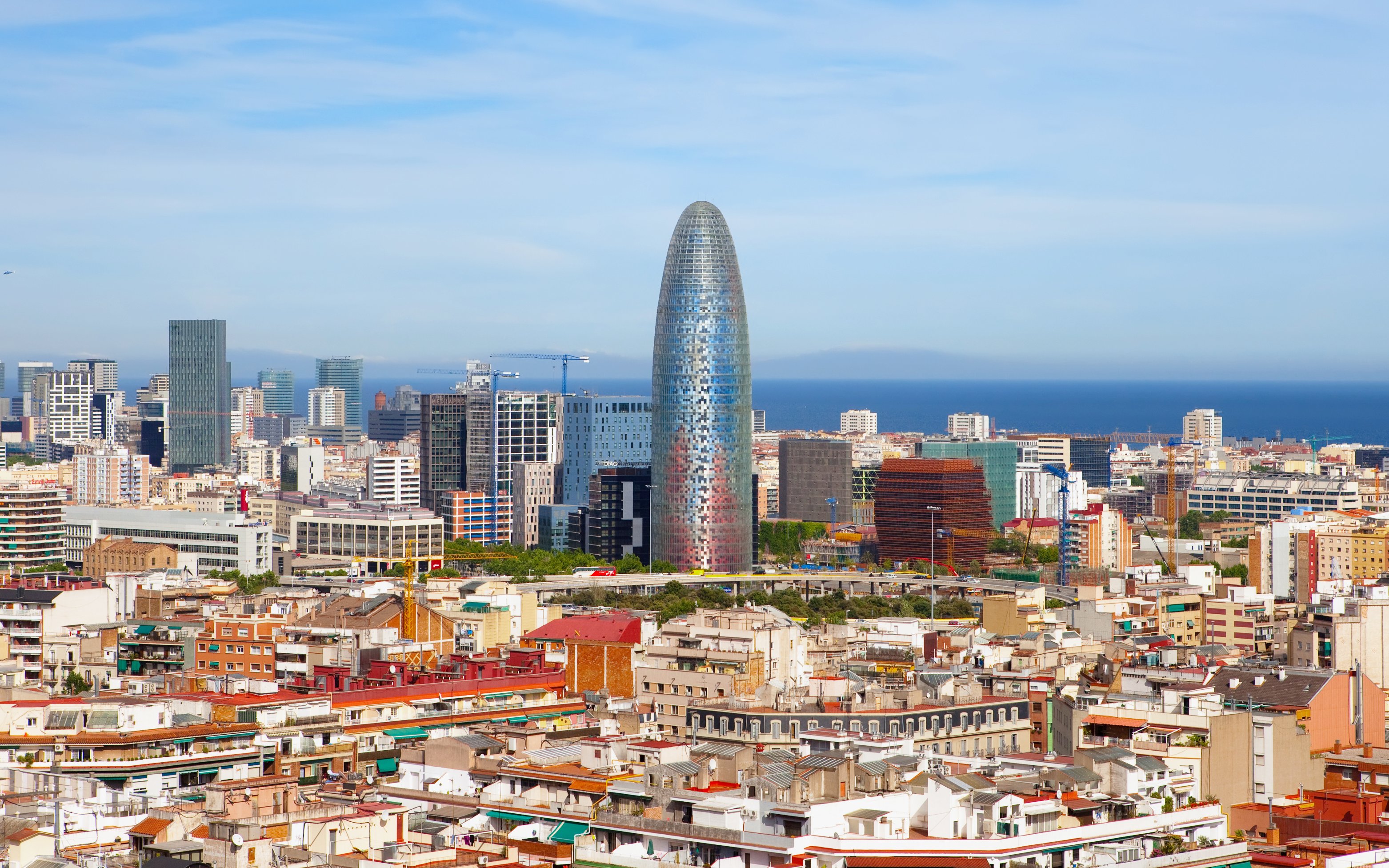 Aerial view of Barcelona featuring Torre Glòries with cityscape and sea in the background.