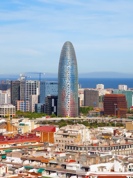 Aerial view of Barcelona featuring Torre Glòries with cityscape and sea in the background.