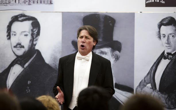 Opera singer performing in front of portraits at Opera's Greatest Hits concert.