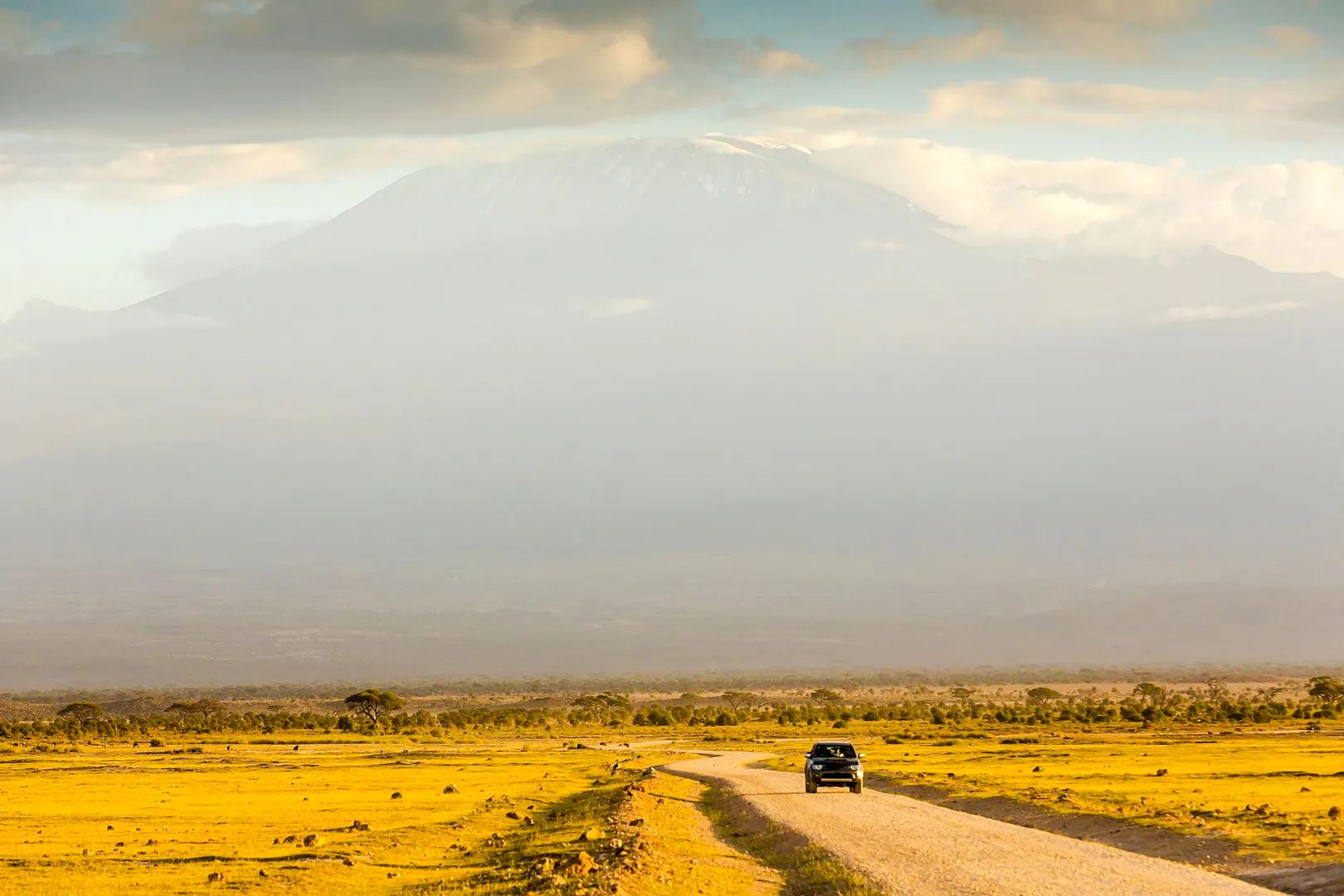 Car on a dirt road with Mount Kilimanjaro in the background, Amboseli National Park.