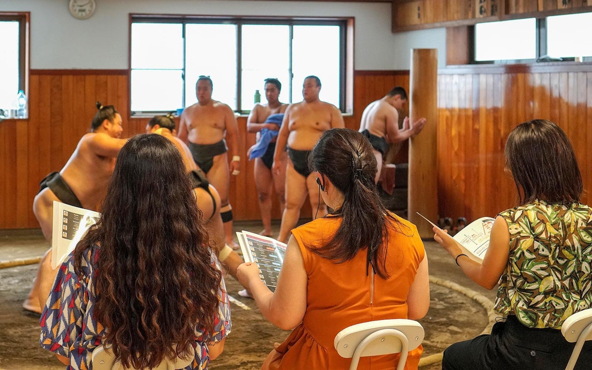 Sumo wrestlers practicing in a stable with spectators observing in Tokyo.