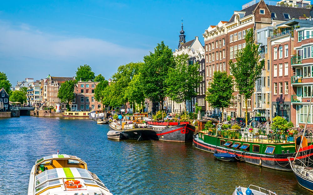 Boat cruising through Amsterdam Canal with historic buildings in the background.