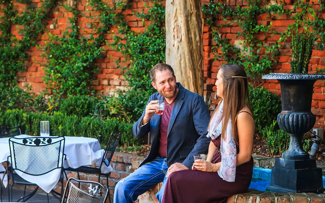 Couple enjoying drinks on New Orleans craft cocktail walking tour in a garden setting.
