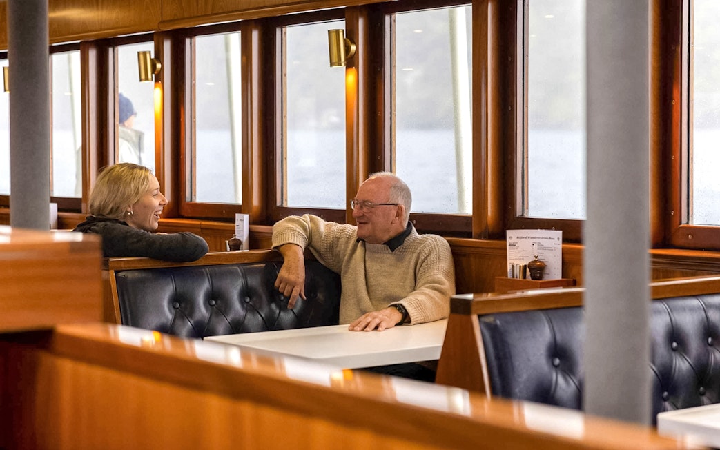 Passengers enjoying conversation in a cozy dining area on Doubtful Sound overnight cruise.