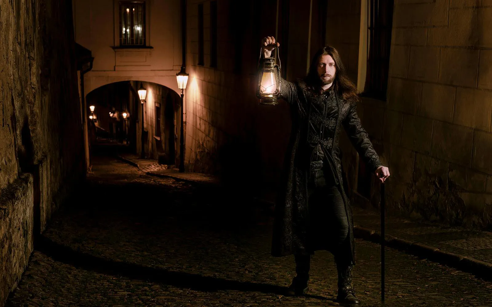 Tour guide holding lantern in dark alley during Prague Old Town ghost tour.