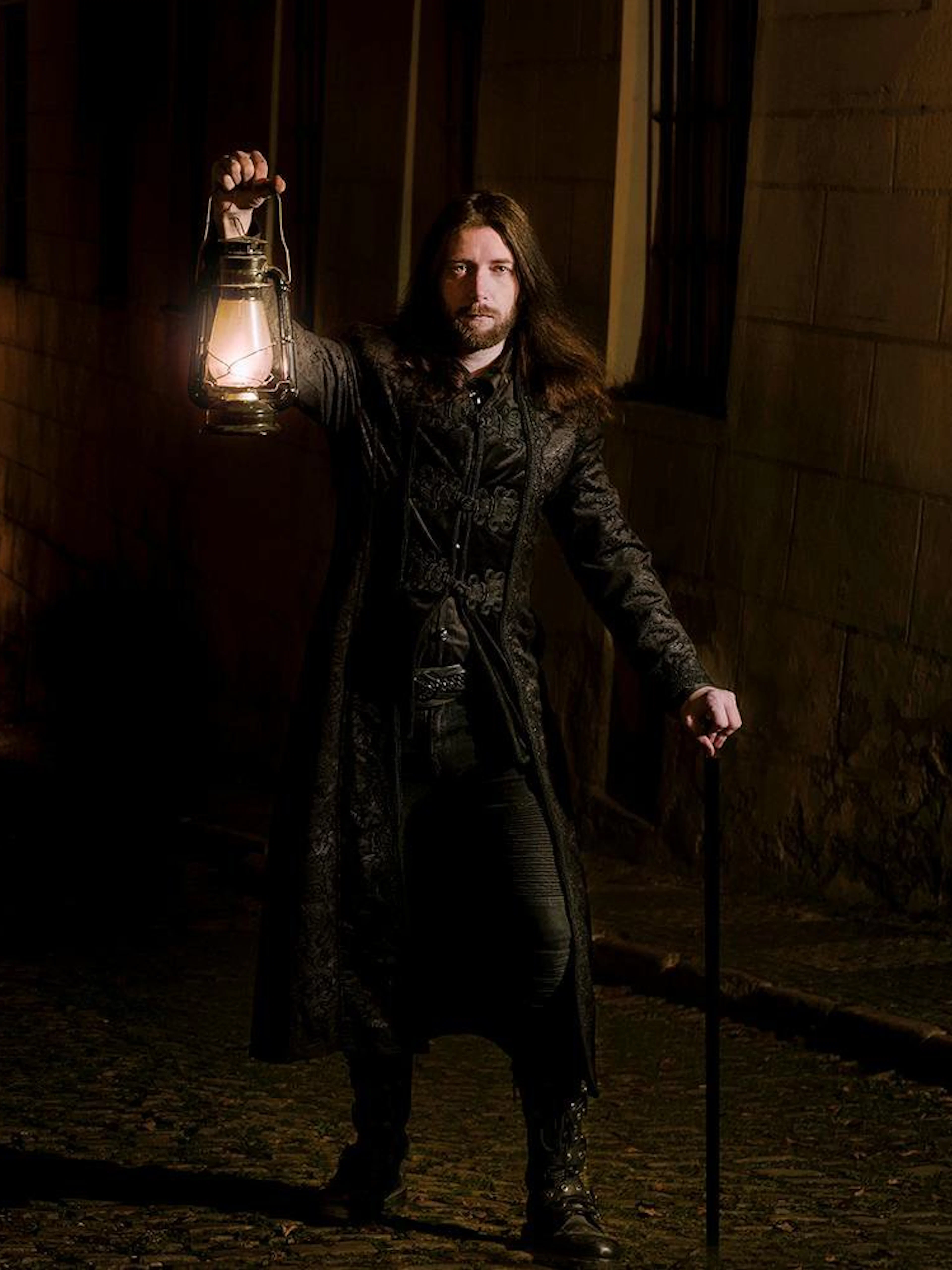 Tour guide holding lantern in dark alley during Prague Old Town ghost tour.