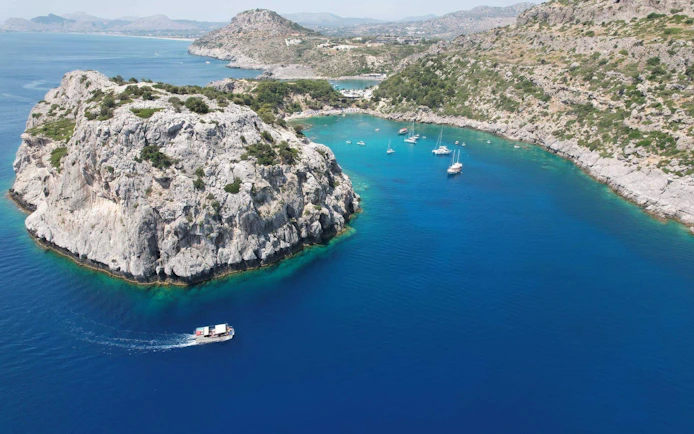 Boats sailing near rocky coastline on the coast of Rhodes, Greece.