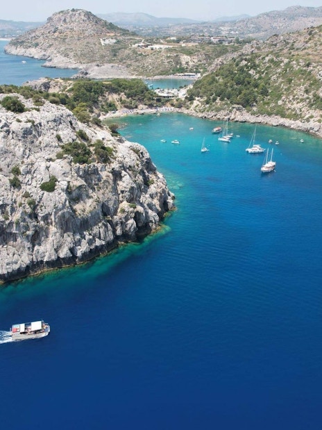 Boats sailing near rocky coastline on the coast of Rhodes, Greece.