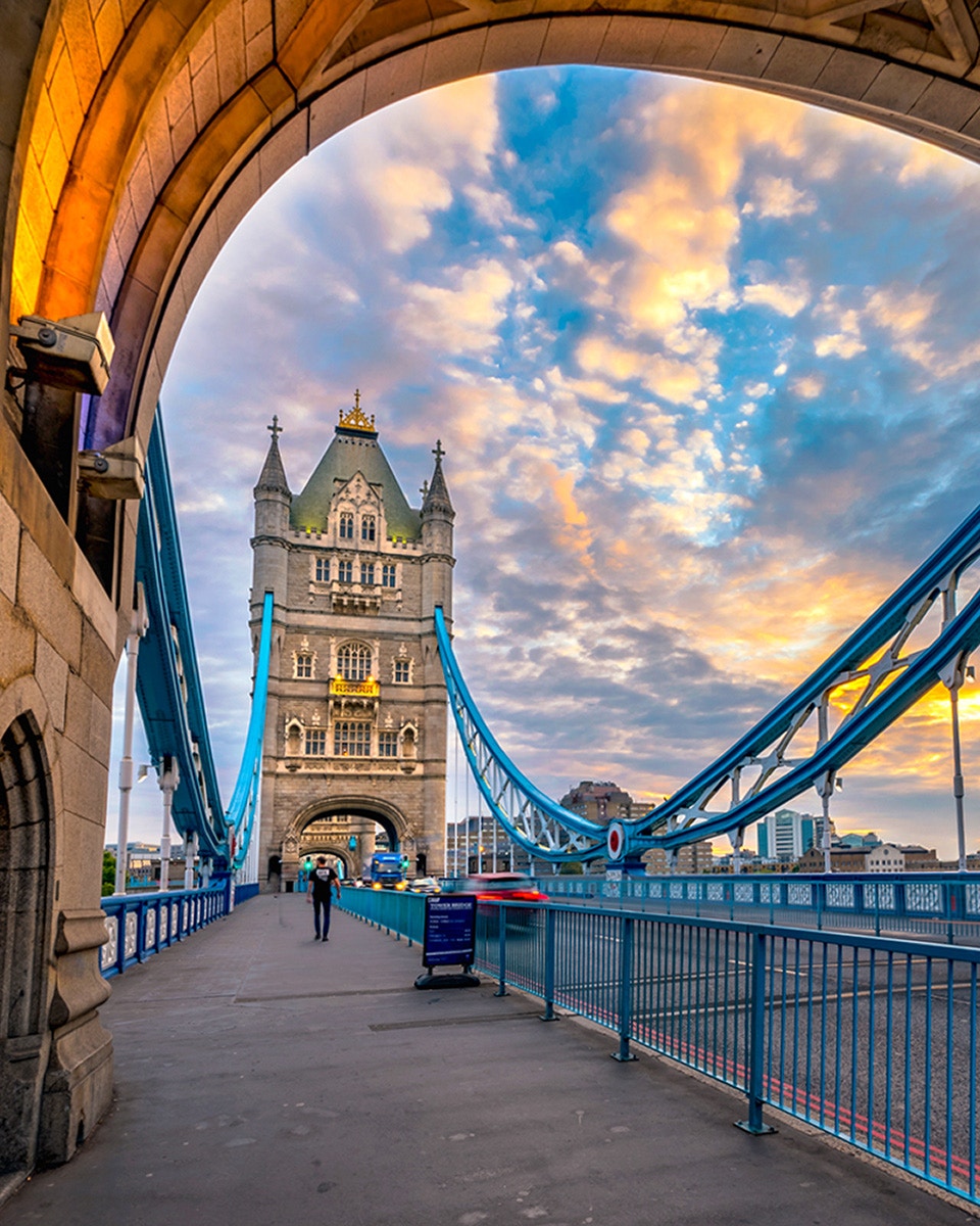 Tower Bridge in London at sunset with a pedestrian walking across.