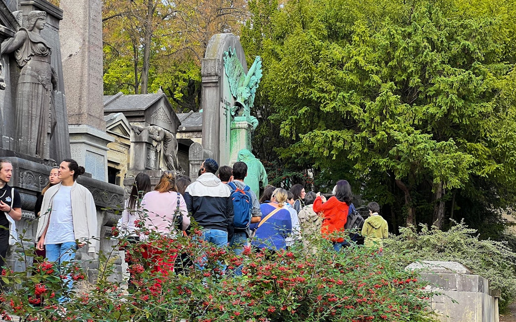 Visitors exploring statues and tombs at Père Lachaise Cemetery, Paris.