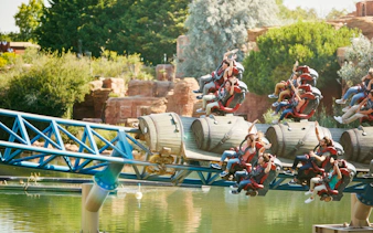 Riders on Furius Baco roller coaster at PortAventura over water.