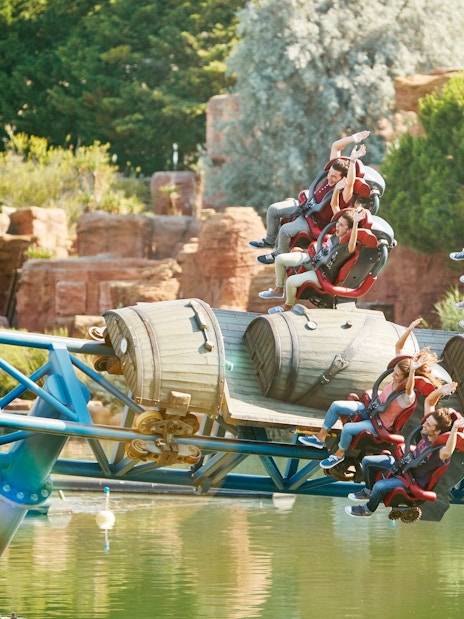 Riders on Furius Baco roller coaster at PortAventura over water.
