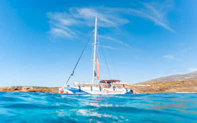 Catamaran sailing near rocky coastline on a whale and dolphin watching cruise.