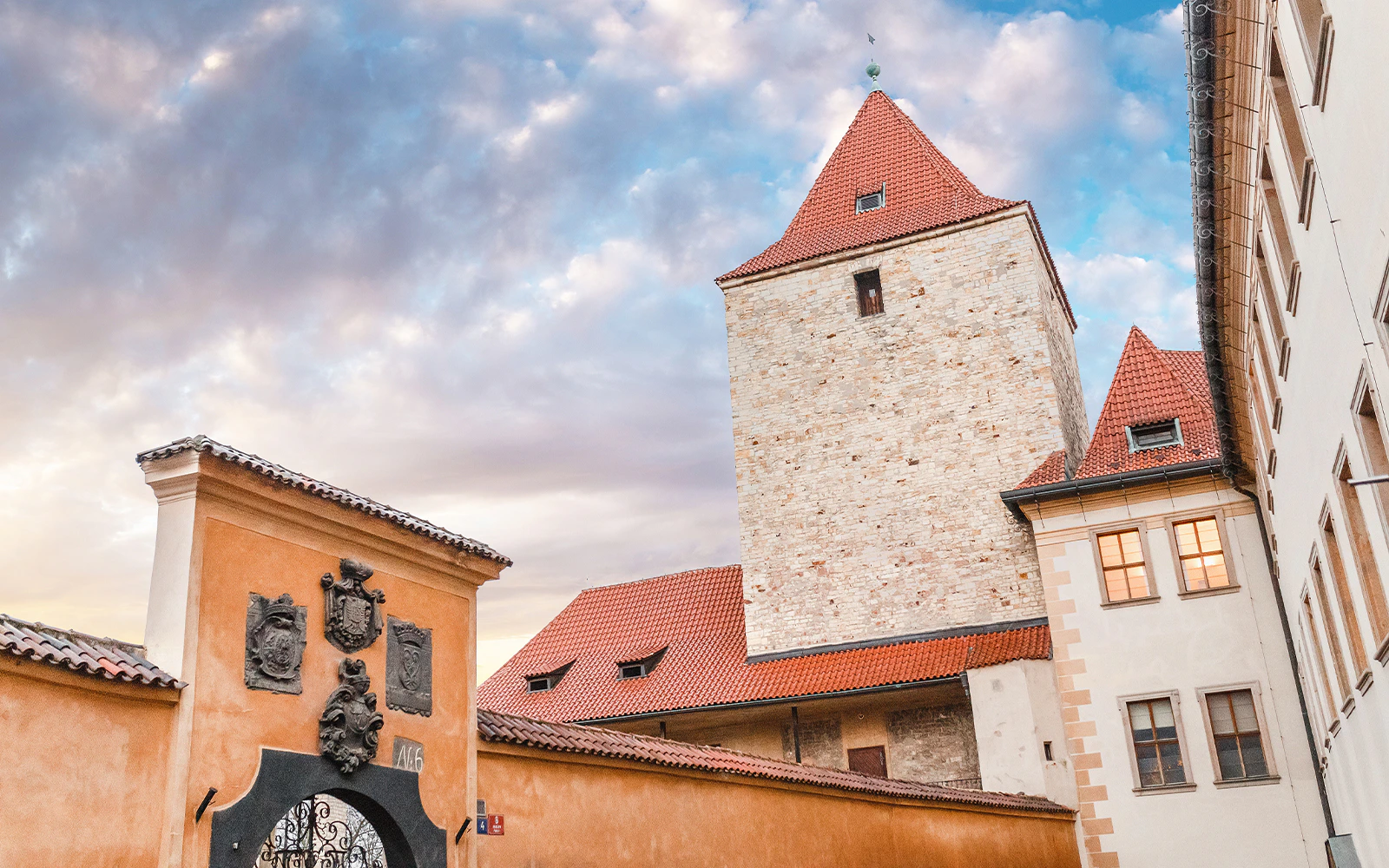 Daliborka Tower at Prague Castle with red-tiled roofs under a cloudy sky, Czech Republic.