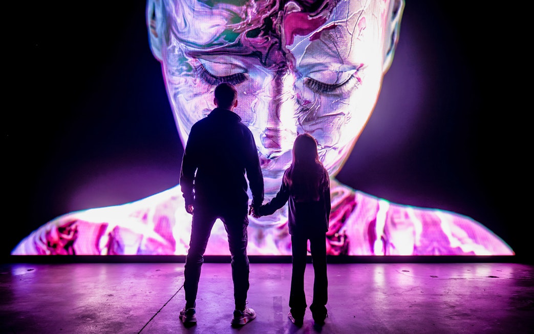 Visitors at AMAZE Amsterdam viewing a large digital face display.