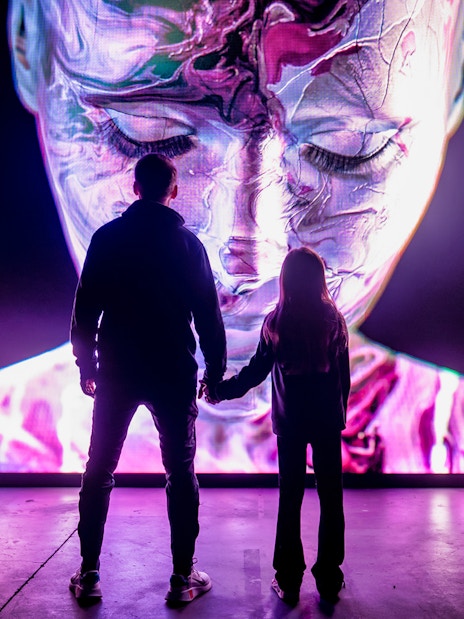 Visitors at AMAZE Amsterdam viewing a large digital face display.