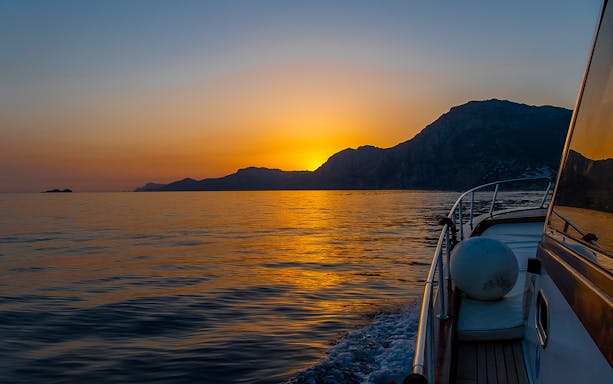 Boat cruising along the Amalfi Coast at sunset, Italy.