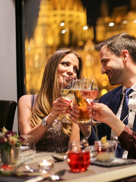 Guests toasting on a Budapest dinner cruise with a piano battle show in the background.