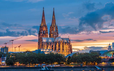 Cathedral of Cologne at sunset with illuminated spires and colorful sky.