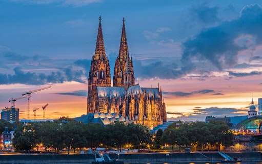 Cathedral of Cologne at sunset with illuminated spires and colorful sky.